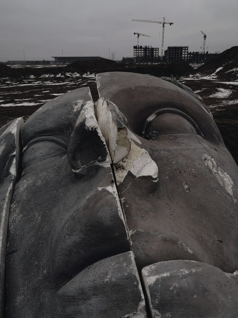 The Return of the Dead God: The Decaying Idol of Humanism. Statue of face broken into pieces. Background desolate industrial zone. Credit: https://www.pexels.com/@octoptimist/